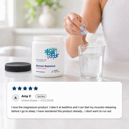 Person holding a supplement container labeled 'Bluegrass Supplements Maximum Magnesium' with a glass of water on a marble surface.